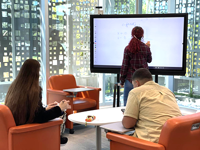 Una estudiante brindando tutoría en el edificio del Learning Commons, escribiendo en una pizarra electrónica.