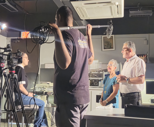 Durante la grabación de un documental, una mujer y un hombre son entrevistados en un laboratorio, mientras el equipo técnico graba con cámaras y micrófono tipo pértiga.