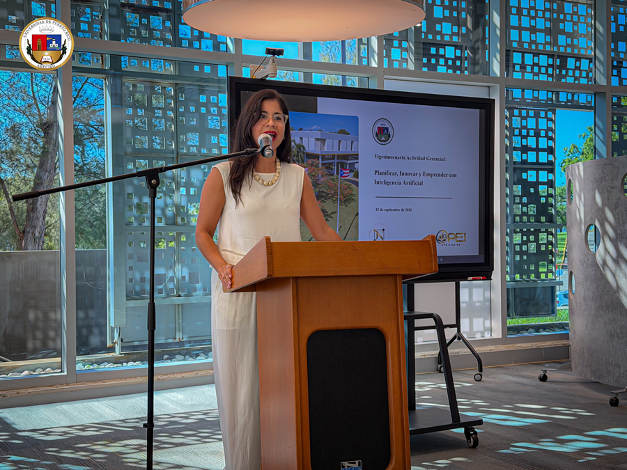 Una mujer habla ante un micrófono detrás de un podio de madera durante la Actividad Gerencial #24 de la Universidad de Puerto Rico en Arecibo. Detrás de ella, una pantalla presenta el tema “Planificar, Innovar y Emprender con Inteligencia Artificial” y la fecha 25 de septiembre de 2026.